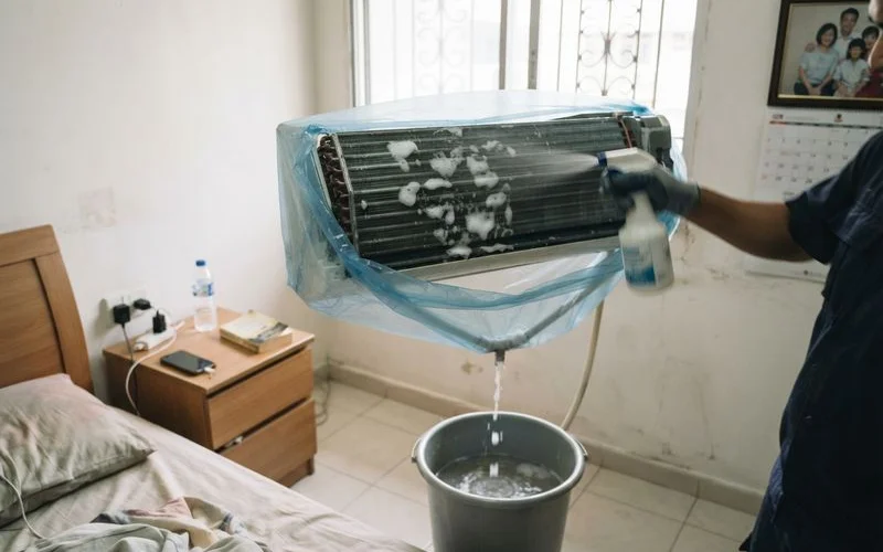 A technician performing a chemical wash on the dismantled indoor components of a split-unit air conditioner in Singapore